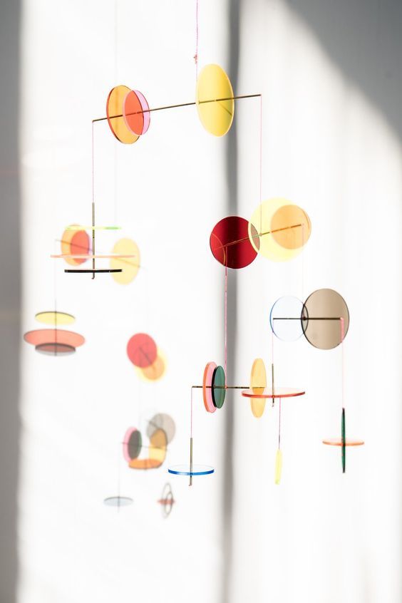 an abstract mobile is hanging from the ceiling in front of a window with sunlight streaming through it