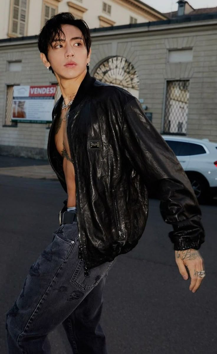 a shirtless man in jeans and a leather jacket is walking down the street with his hand on his hip