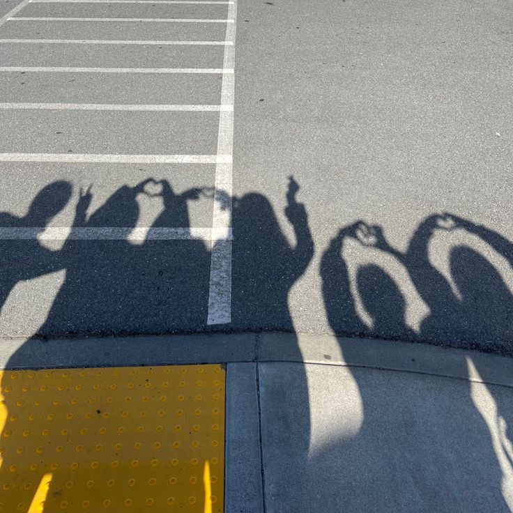 the shadow of several people holding their hands up in front of an empty parking lot