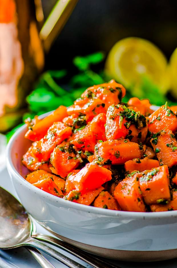 a white bowl filled with cooked carrots next to lemon wedges and silverware