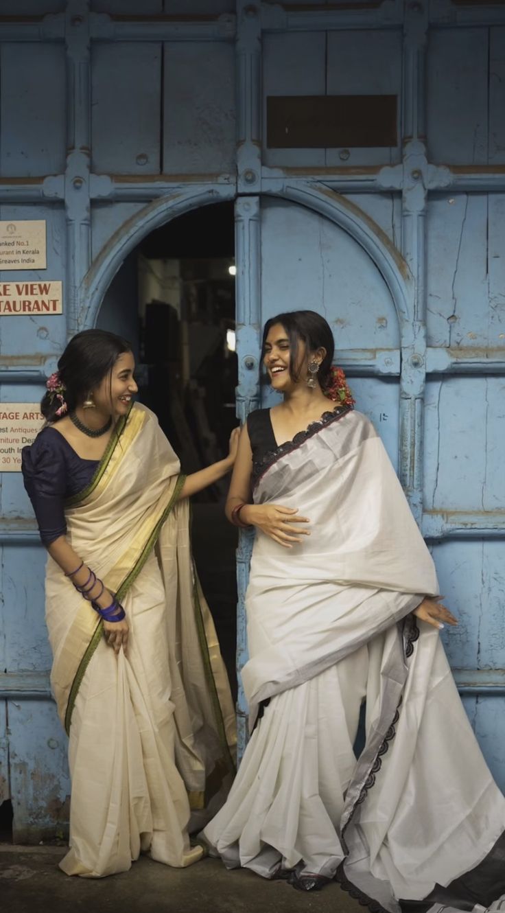 two women standing in front of a blue door with white and black sari on