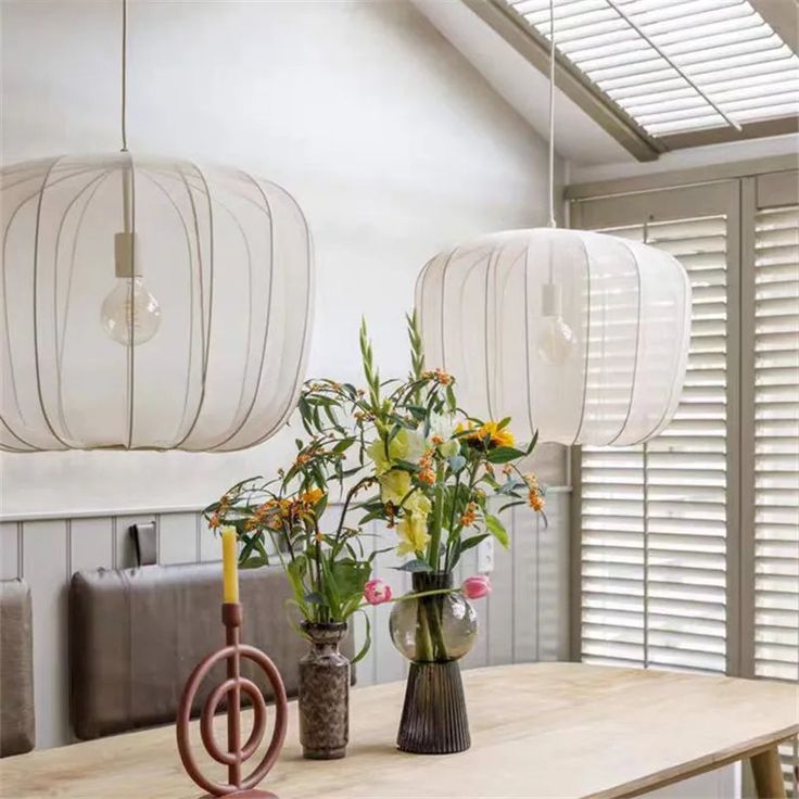 two vases filled with flowers sitting on top of a wooden table next to lamps