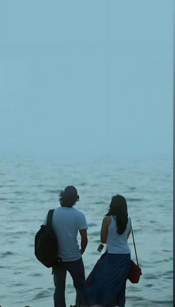 two people standing on the beach looking out at the water