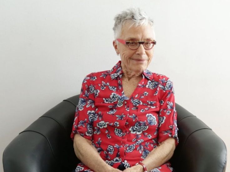 an older woman sitting in a chair with her hands crossed and looking at the camera