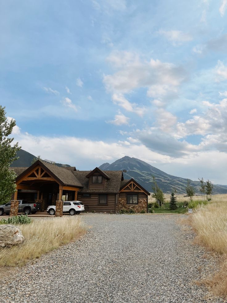 a truck parked in front of a large log cabin on gravel road next to grass and trees