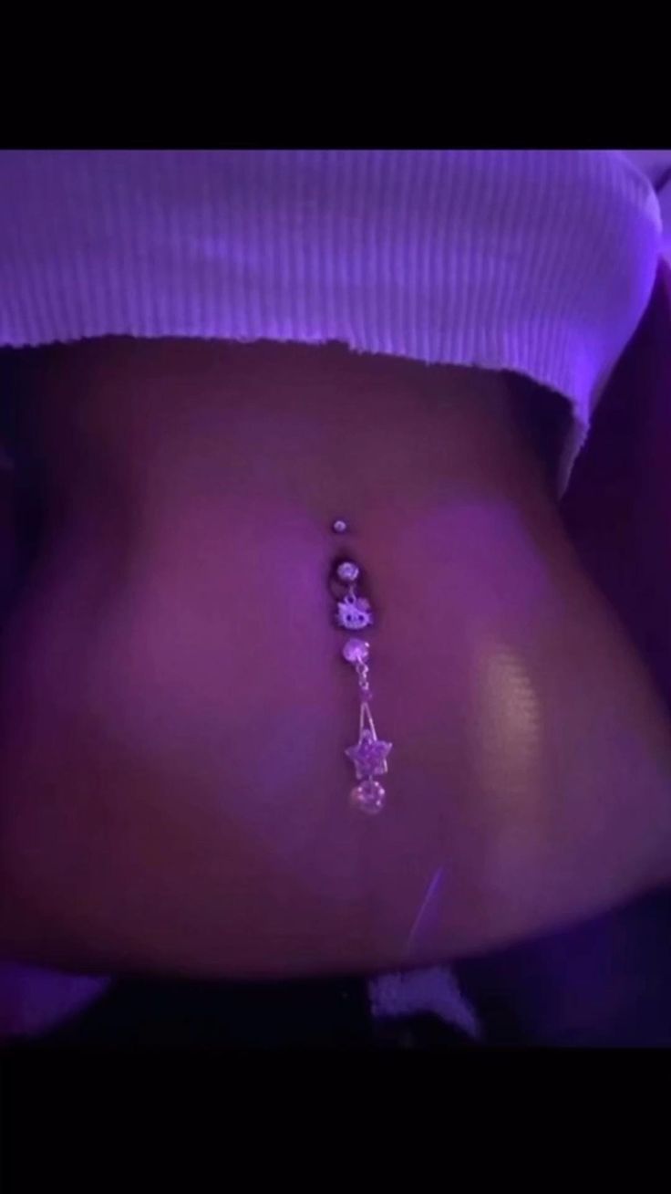 a woman's stomach with a purple glow behind her belly chain and dangling earrings