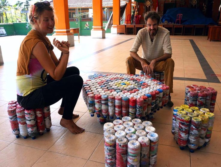 two people sitting on stools made out of cans and cans of soda in front of them