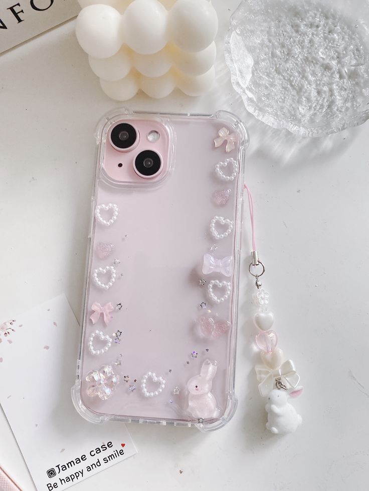 an iphone case with pearls and bows on it sitting next to a pair of earrings