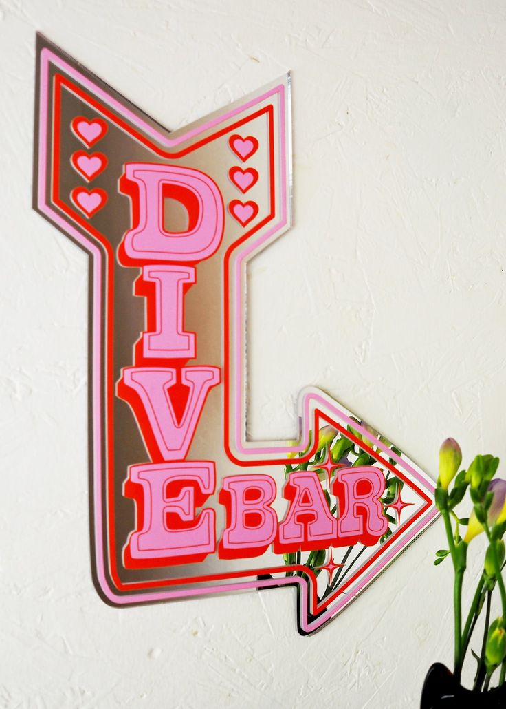 a sign that says dive bar with flowers in the vase on the wall behind it