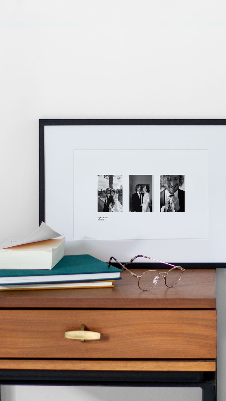 a wooden desk topped with books and glasses next to a framed photo on top of it