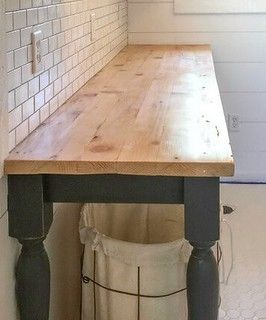 a wooden table sitting under a window next to a white brick wall in a kitchen