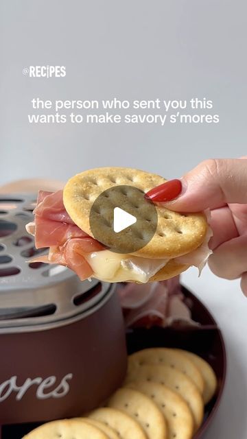 a person holding a sandwich in their hand with crackers on the plate next to it