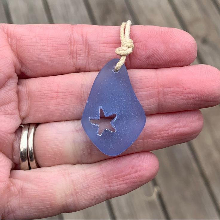 a hand holding a blue sea glass pendant with a star on it's side