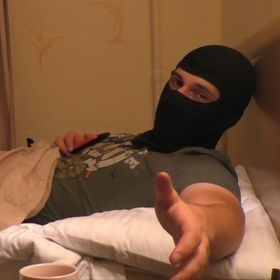 a man in a black mask is laying on a bed and giving the thumbs up