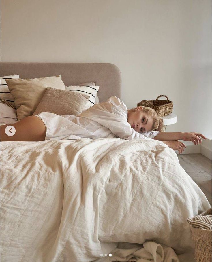 a woman laying on top of a bed in a bedroom next to a basket and pillows