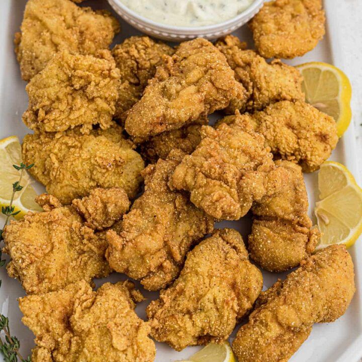 fried chicken on a plate with lemon wedges and ranch dressing in the background,