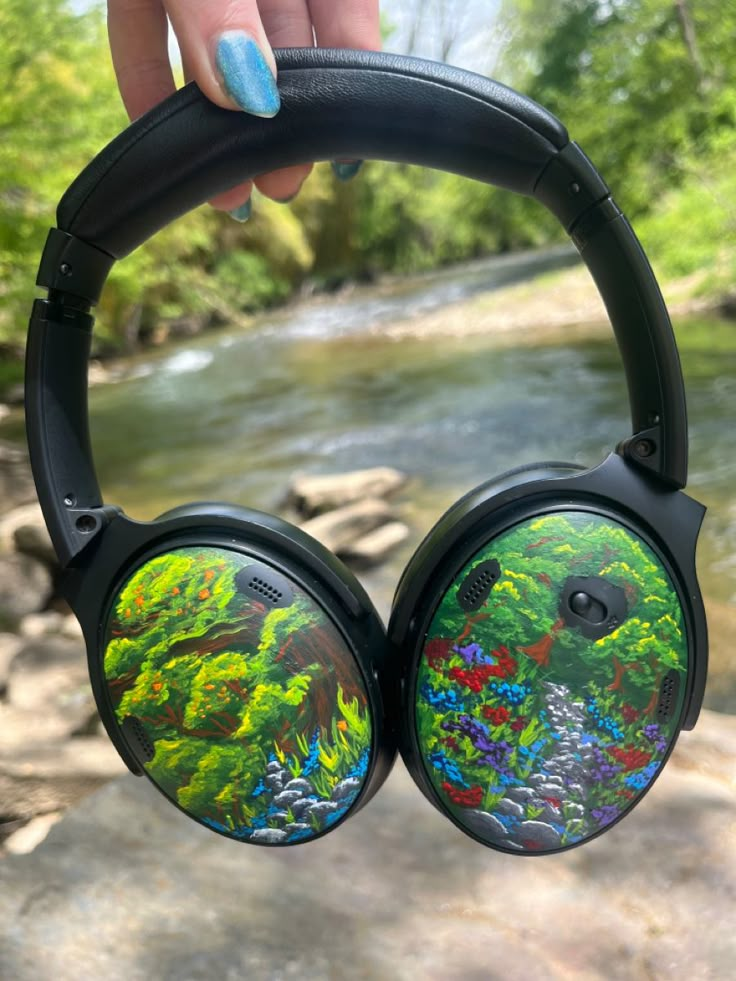 a pair of headphones that are sitting in front of a river with trees and flowers on them