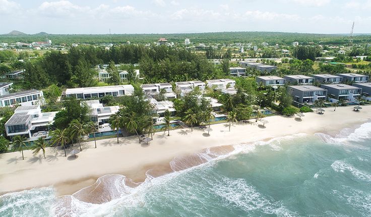 an aerial view of the beach and ocean in front of several houses on stilts