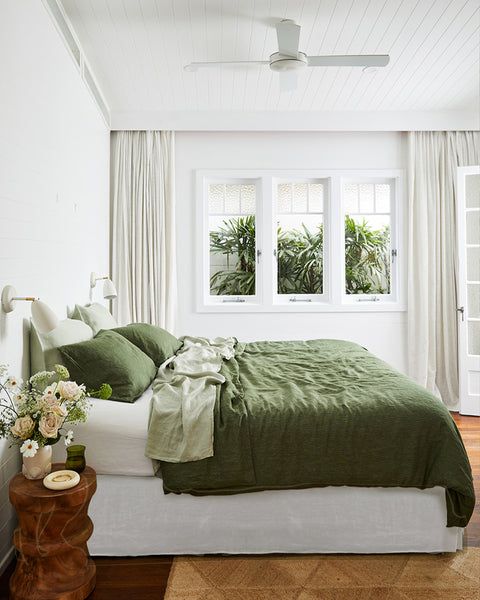 there is a bed with green sheets and pillows in the room that has white walls