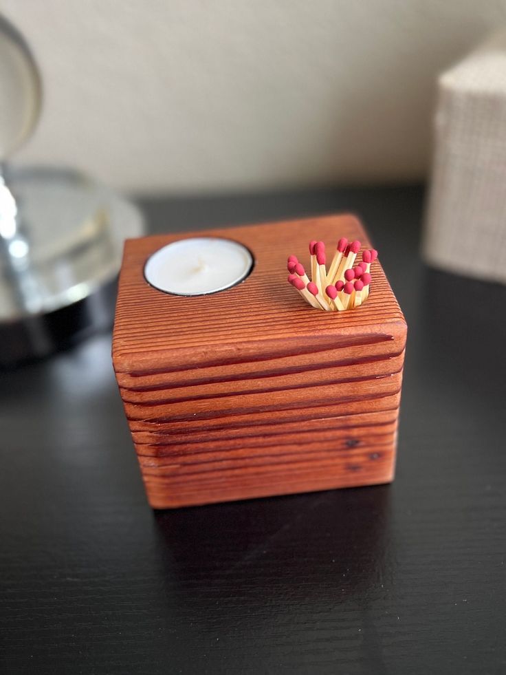 a small wooden box with some red flowers on it sitting on a table next to a candle