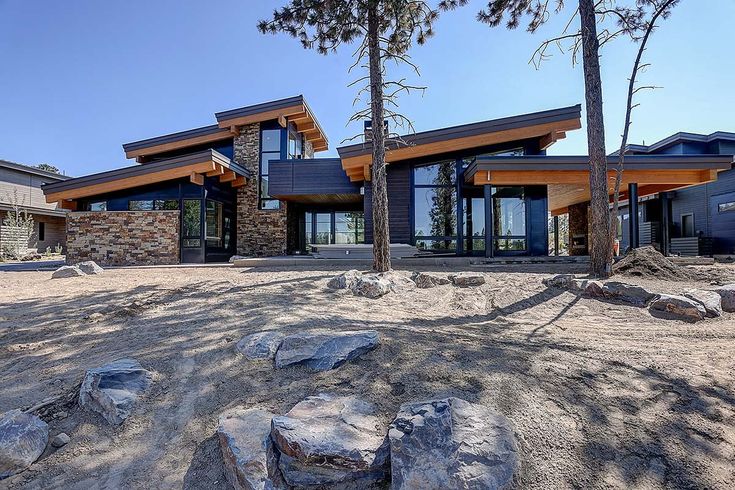 a large house sitting in the middle of a forest filled with trees and rocks on top of a dirt field