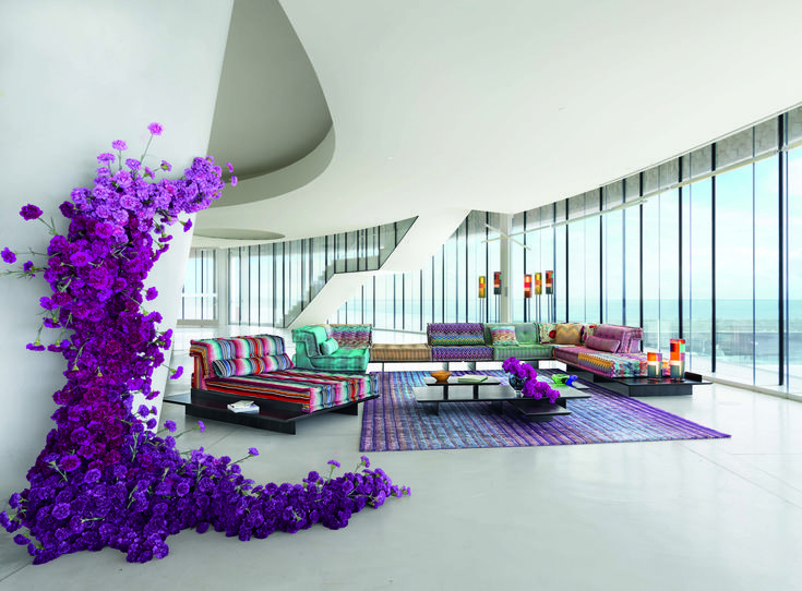 a living room filled with furniture and lots of purple flowers on the floor next to tall windows