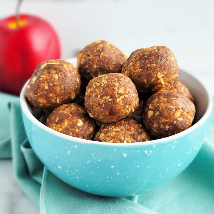 a blue bowl filled with granola balls on top of a table next to an apple