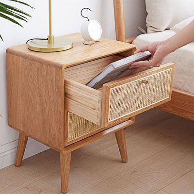 a person holding a remote control in their hand near a bed with a wooden night stand