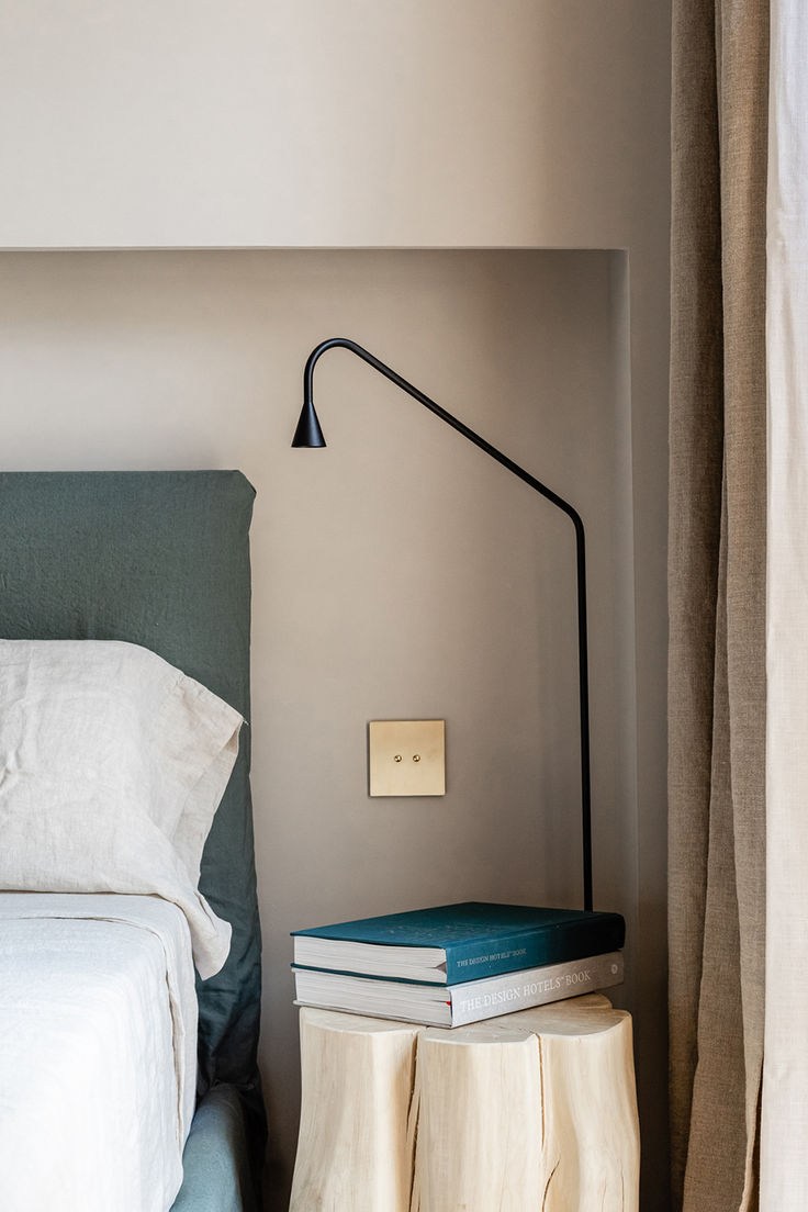 a bed sitting next to a nightstand with two books on it and a lamp in the corner