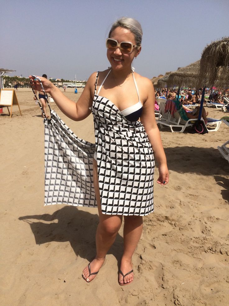 a woman in a black and white dress holding up a towel on the beach while wearing sunglasses