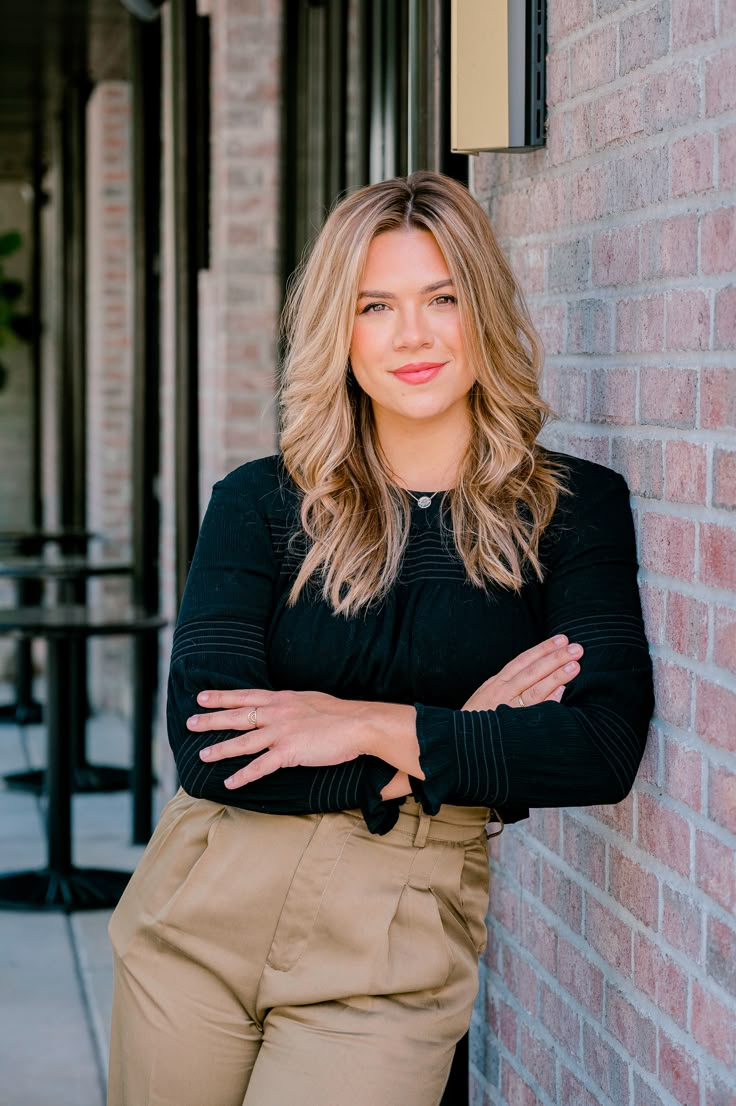 a woman leaning against a brick wall with her arms crossed and looking at the camera