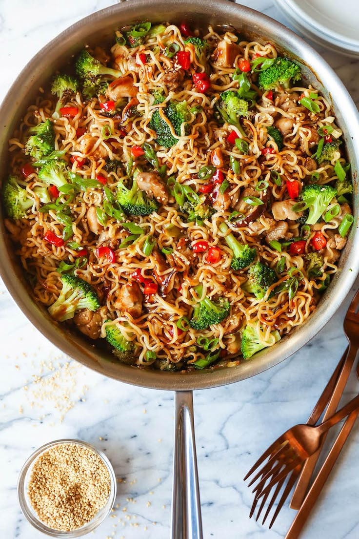 a pan filled with noodles and broccoli on top of a marble countertop