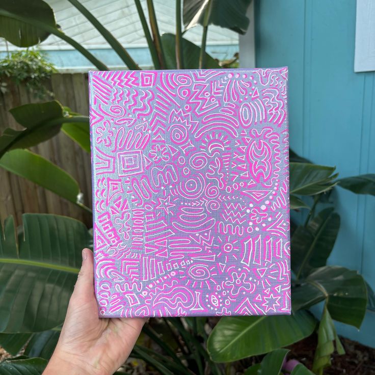 a person holding up a pink and white square with designs on it in front of some plants