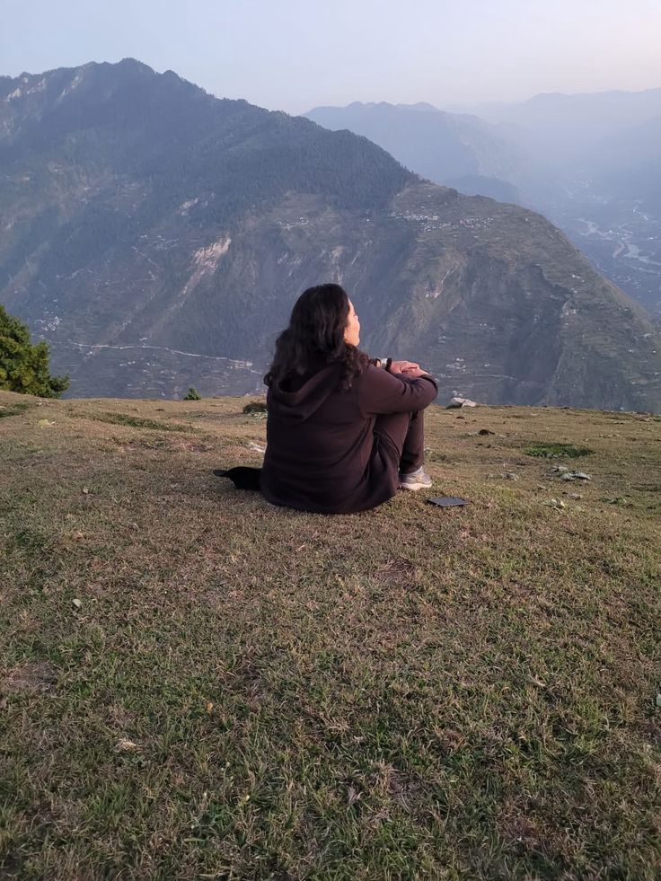 a woman sitting on top of a grass covered hillside