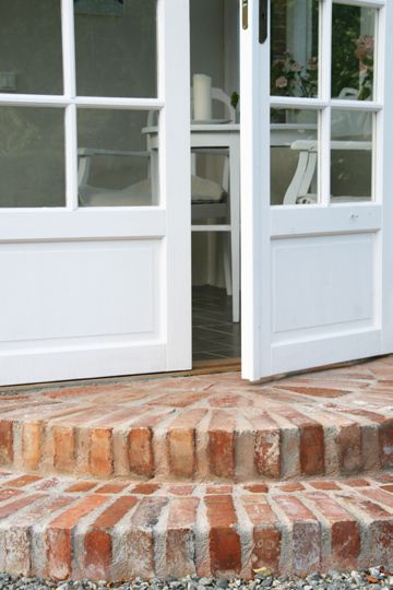 a cat is sitting on the steps in front of an open door and looking outside