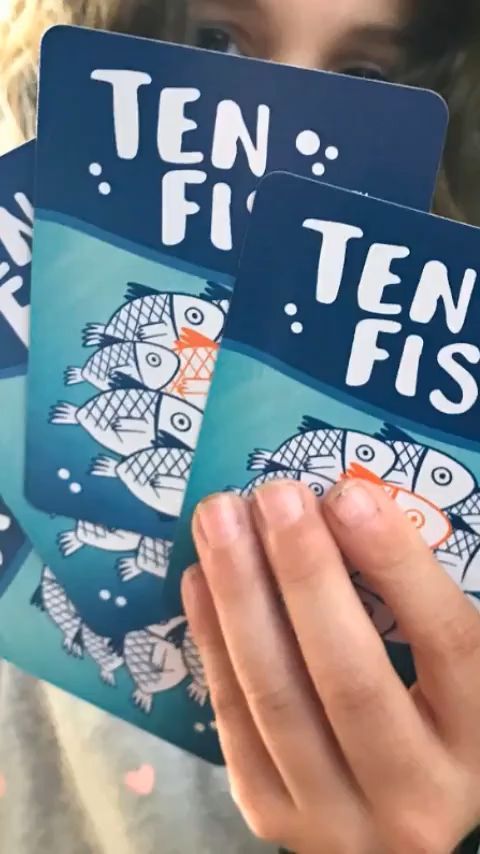 a person holding up three cards with fish on them and the words ten fishes written in white