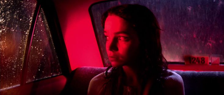 a woman sitting in the back seat of a car with rain coming down on her