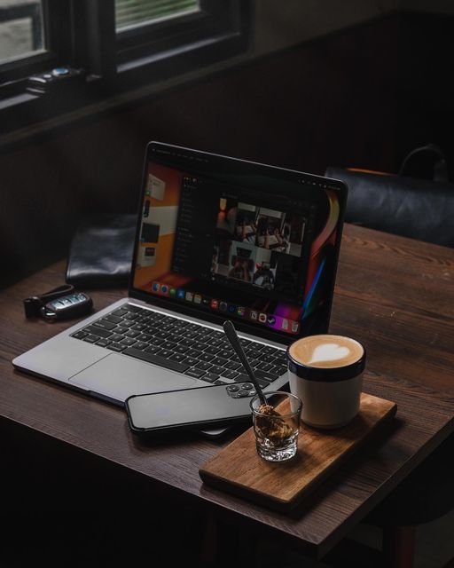 an open laptop computer sitting on top of a wooden desk next to a cup of coffee