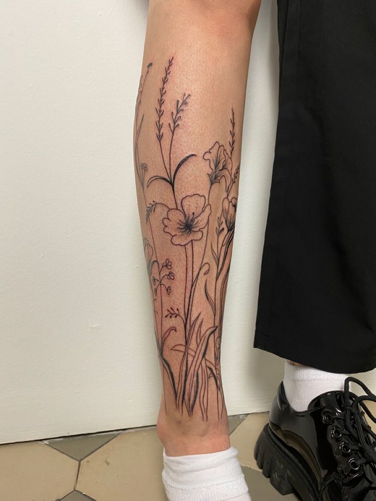 a person standing next to a wall with a flower tattoo on their leg and foot