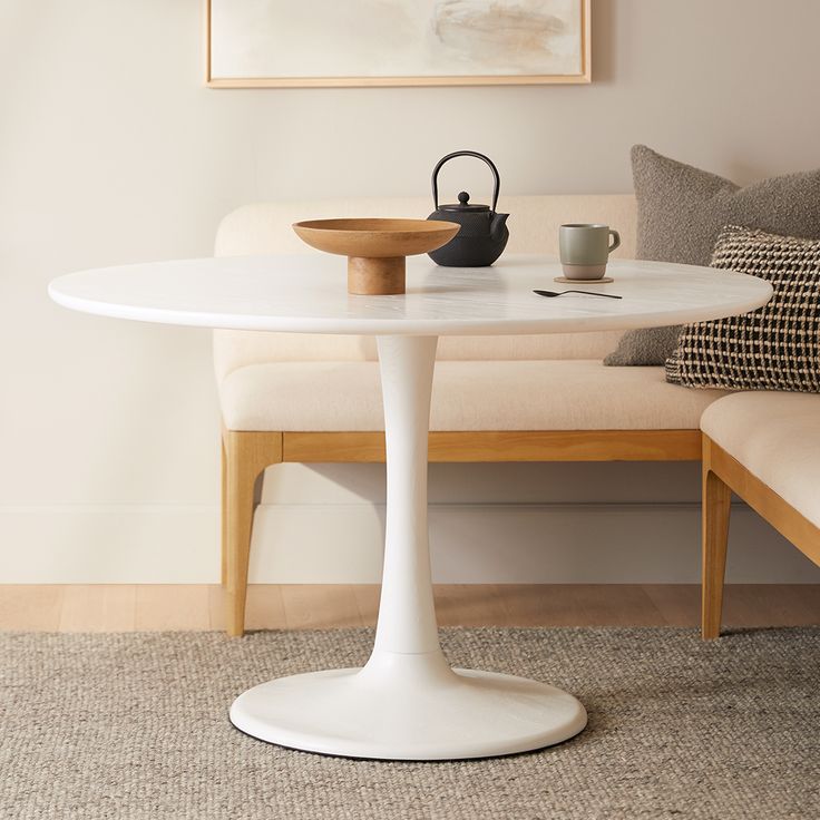 a white table with a black tea pot on it in front of a beige couch