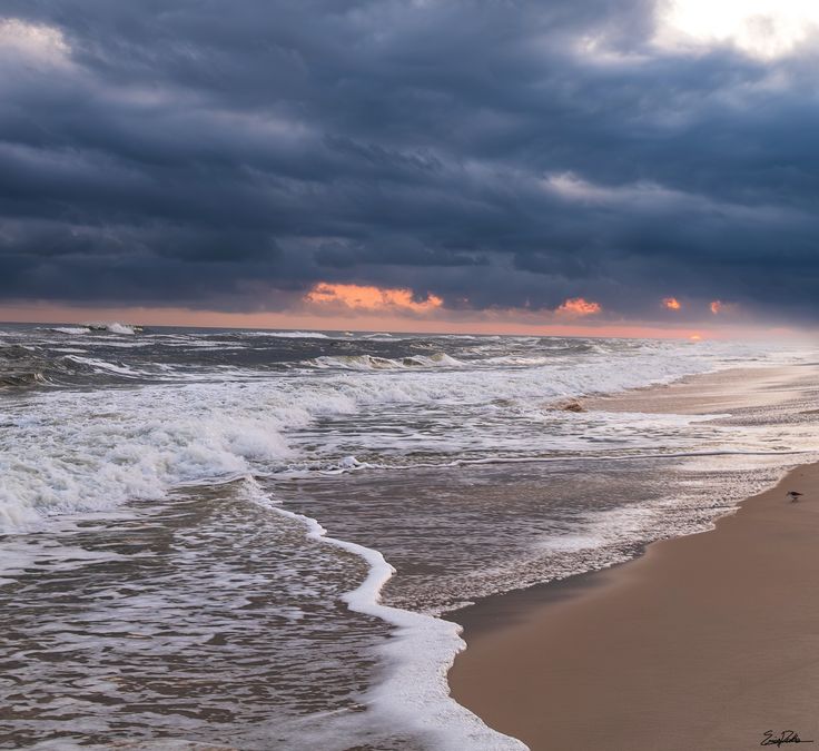 an ocean beach with waves crashing on the sand and dark clouds in the sky above