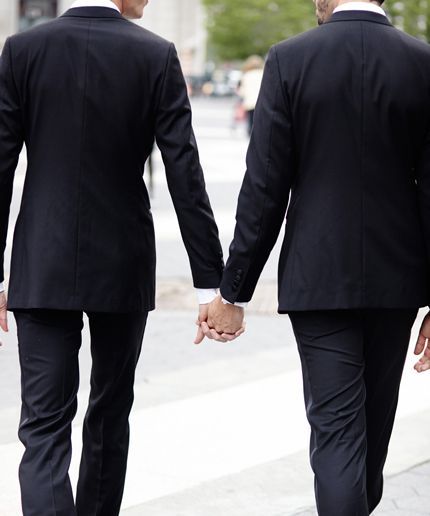 two men in suits walking down the street holding hands