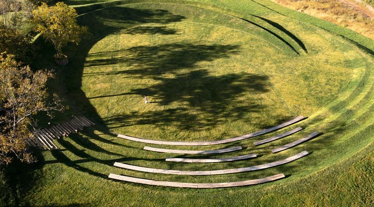 an aerial view of a circular grassy area with benches on the grass and trees in the background