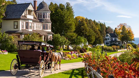A horse and buggy outside a victorian style house along the coast of Mackinac Island with lush greenery around it (Credit: Mackinac Island Tourism Board)