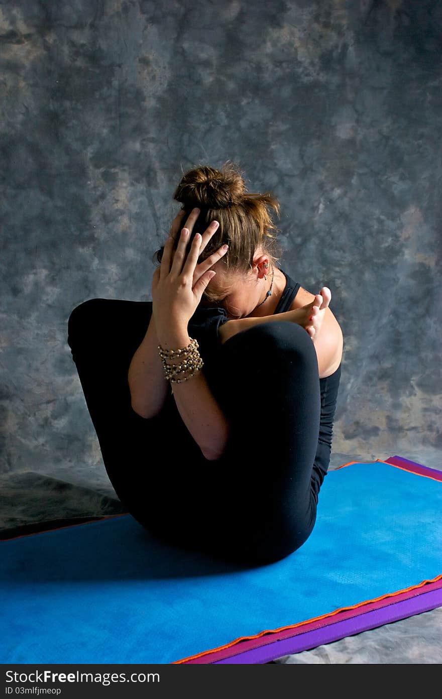 A brown haired caucasian woman is doing yoga exercise, Womb Embryo Posture or Garbha Pindasana posture studio on yoga mat with grey mottled background. A brown haired caucasian woman is doing yoga exercise, Womb Embryo Posture or Garbha Pindasana posture studio on yoga mat with grey mottled background.