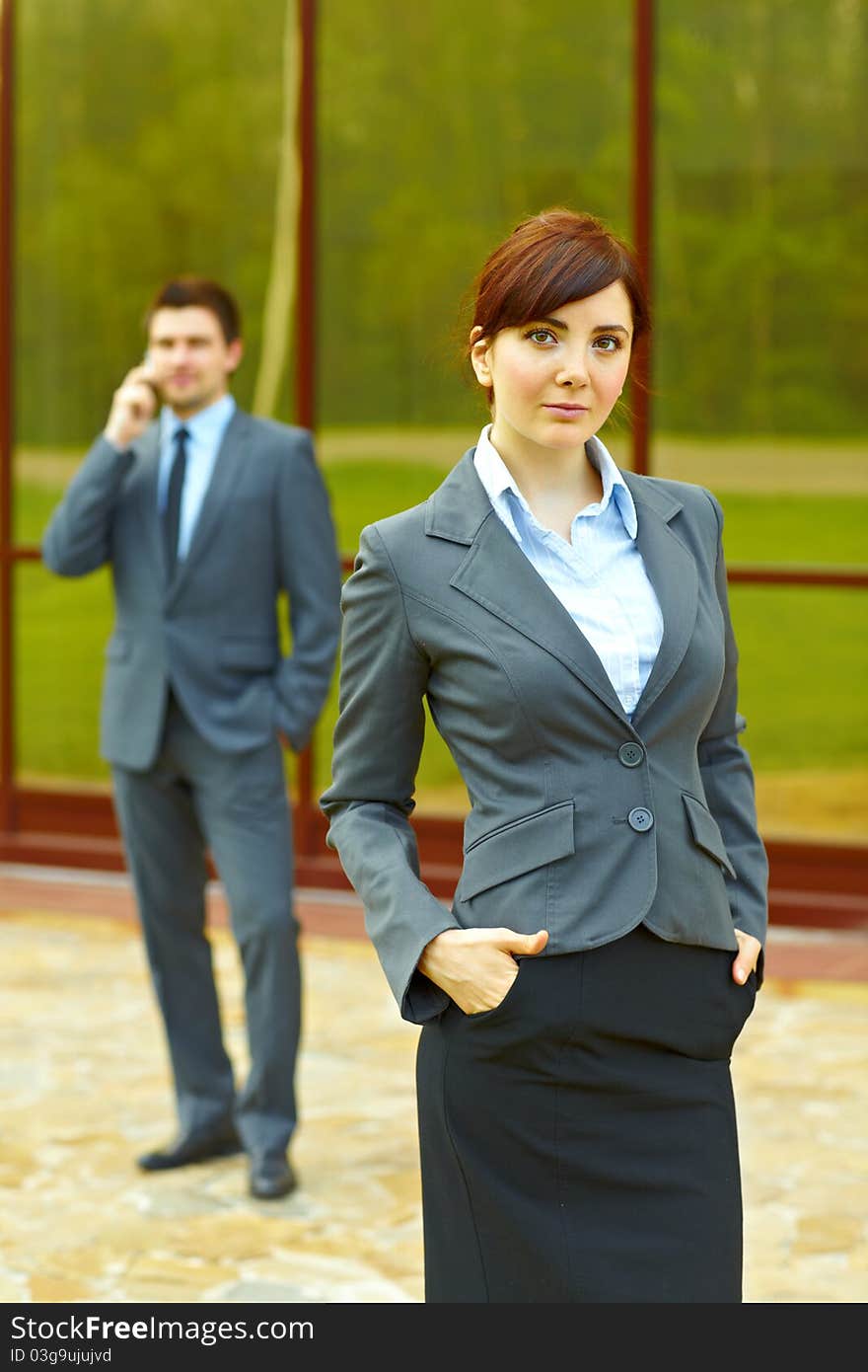 Businessman posing in front of business building and businesswoman in the background talking on the phone. Businessman posing in front of business building and businesswoman in the background talking on the phone