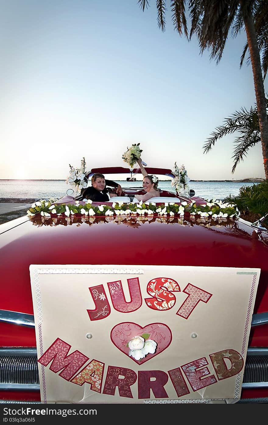 Bride and groom sitting in a red convertible celebrating and overlooking the ocean. Bride and groom sitting in a red convertible celebrating and overlooking the ocean.