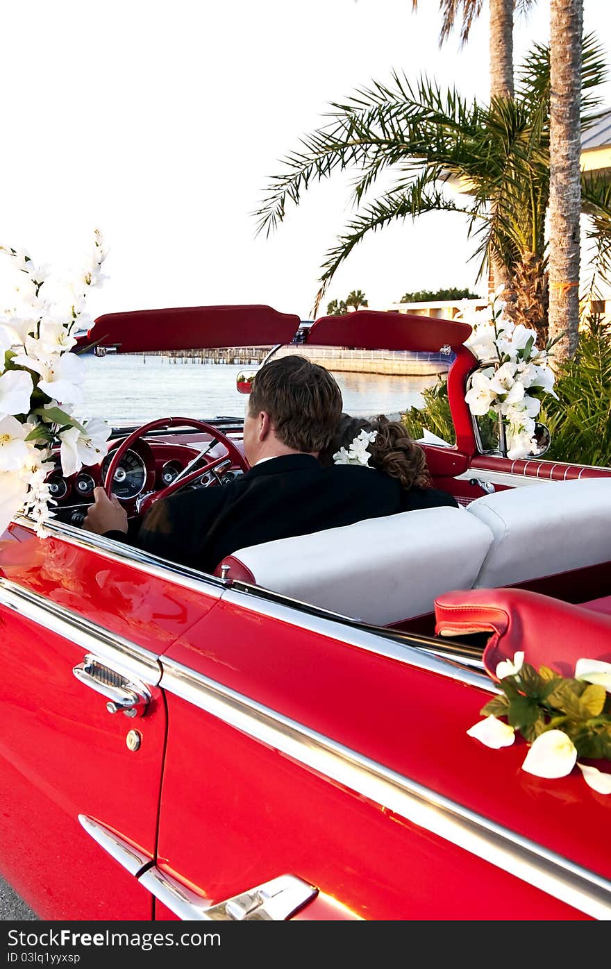 Bride and groom sitting in a red convertible overlooking the ocean. Bride and groom sitting in a red convertible overlooking the ocean.