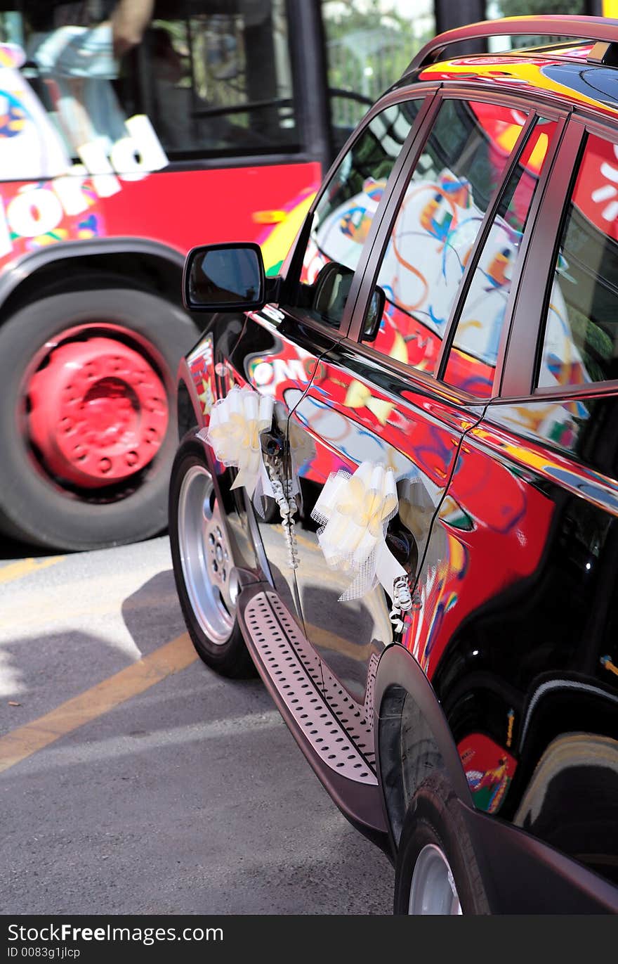 Colourful bus passing black wedding car with ribbons and reflections in the paint