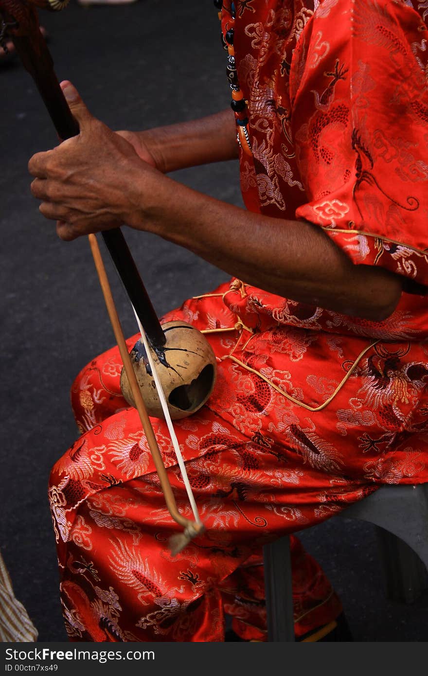 An old man wearing in red playing a Chinese instrument, er wu. An old man wearing in red playing a Chinese instrument, er wu.